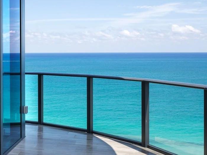 A curved glass balcony guardrail and its top rail above the ocean