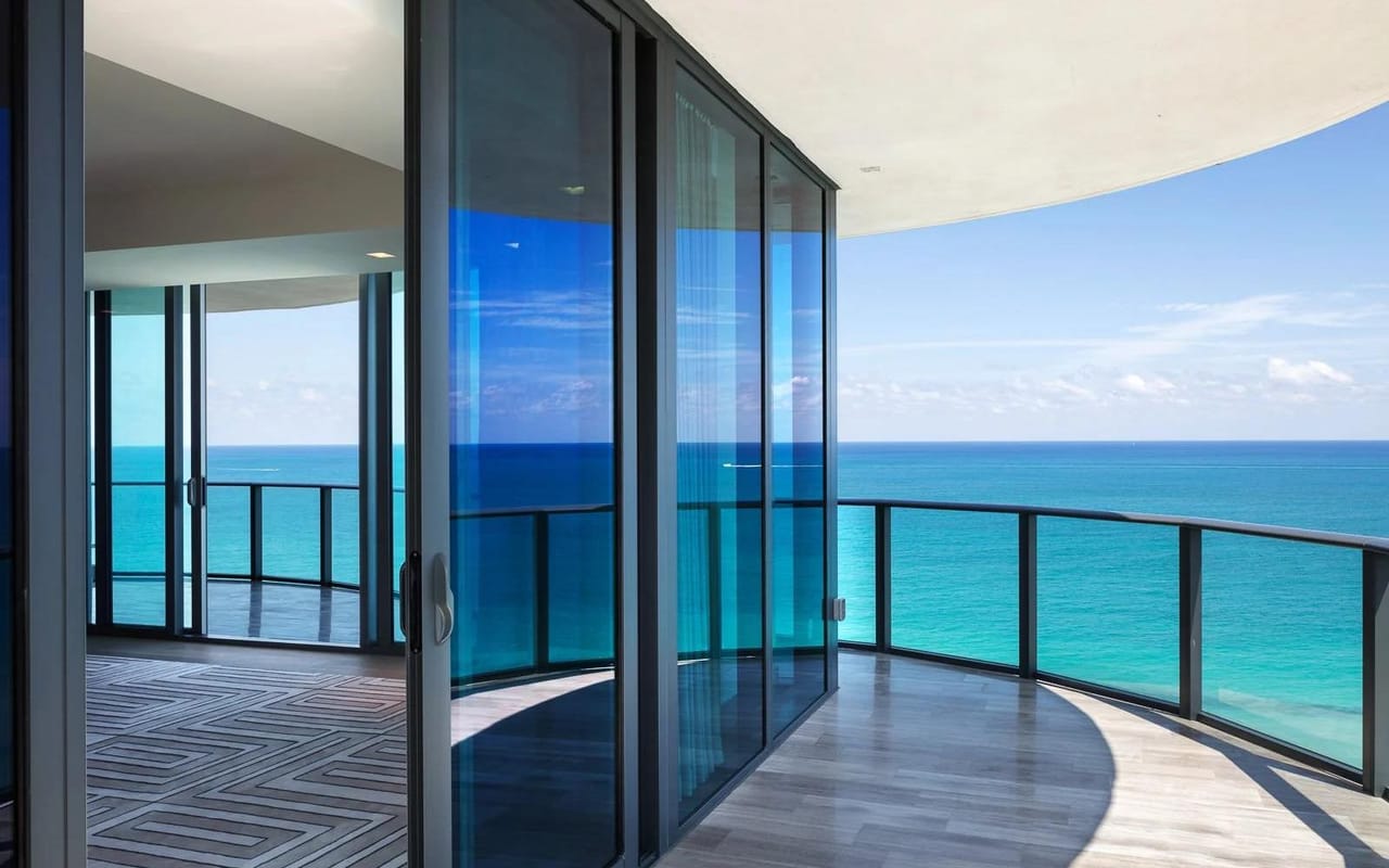 A curved oceanfront condominium balcony with a glass guardrail overlooking the Atlantic